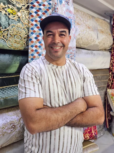 محمد، صاحب محل أفرشة فارس، داخل محله بالخميسات أمام لفائف الأقمشة